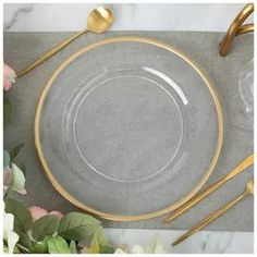 a glass plate with gold rim and two golden spoons next to it on a marble table