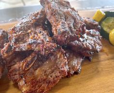 some meat is sitting on a cutting board next to lemons and cucumbers