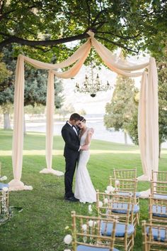 a bride and groom standing under an outdoor wedding ceremony arch with white draping