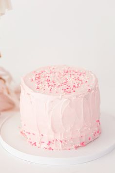 a pink frosted cake with sprinkles on it sitting on a white plate