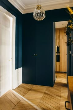 an empty room with blue walls and wood flooring in the center, along with a chandelier hanging from the ceiling