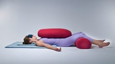 a woman laying on top of a blue and red mat next to a large pillow