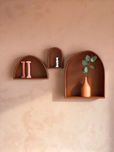 three wooden shelves with vases and figurines on them against a pink wall