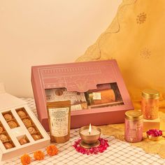 an open pink box with some candles and other items around it on a white table cloth