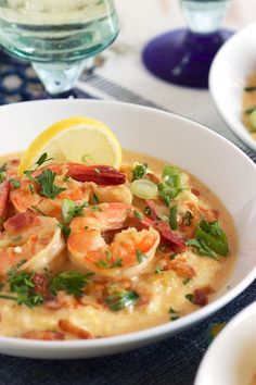 a bowl of soup with shrimp and garnish on the side, next to a glass of wine