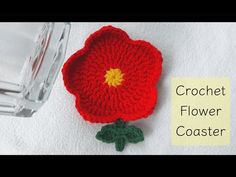 a crochet flower sits next to a glass jar on a white towel with the words crochet flower coaster written below it