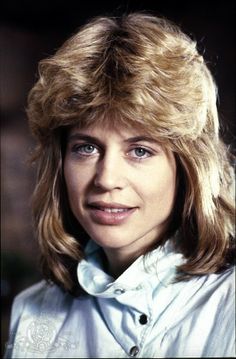 a close up of a person wearing a white shirt and long blonde hair with bangs