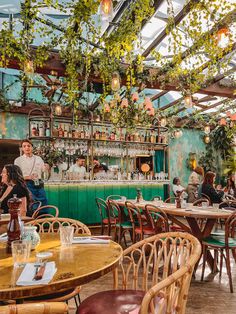 people sitting at tables in a restaurant with plants hanging from the ceiling and green walls