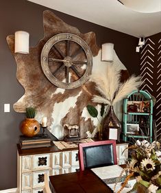 a dining room table with chairs and a cow hide wall hanging on the wall behind it