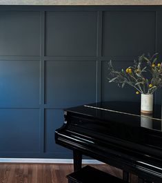 a black piano sitting in front of a blue wall with flowers on top of it