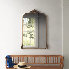 a wooden bench with a hat on it next to a mirror and window in the wall