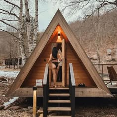 a woman is standing in the doorway of a small wooden cabin with stairs leading up to it