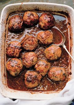 meatballs covered in gravy are being spooned into a casserole dish