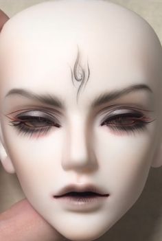 a person holding up a white mannequin's head with black eyebrows and eyeliners