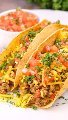 two tacos on a white plate with salsa and sour cream in the back ground