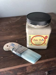 a wooden table with a paint brush and jar of white stuff on top of it