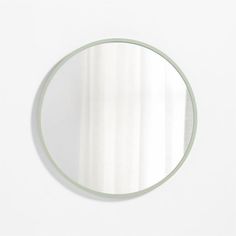 a round mirror hanging on the wall next to a white wall with vertical striped curtains