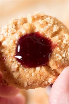 a person holding up a cookie with jelly on it's center and crumbs in the middle