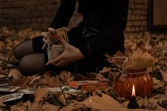 a woman is sitting on the ground surrounded by leaves and books with a lit candle in her hand