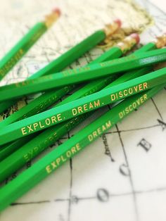 several green pencils sitting on top of a map with the words explore dream discovery written on them