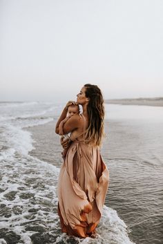 a woman standing in the ocean with her back to the camera and holding onto her baby