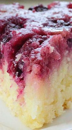 a close up of a piece of cake on a plate with blueberries and raspberry sauce