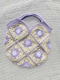 a crocheted purse sitting on top of a gray cloth covered in white and purple yarn