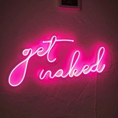 a pink neon sign that says get naked on the side of a wall in a dark room