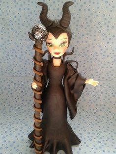 a doll with horns holding a stick and wearing a black dress on a blue background