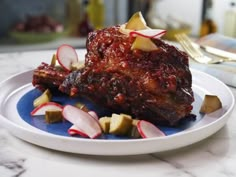 a white plate topped with ribs covered in bbq sauce and sliced radishes