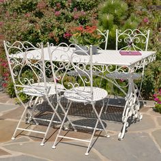 a white table and chairs sitting on top of a stone floor next to flowers in a garden