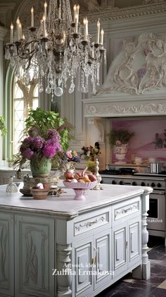 a chandelier hanging from the ceiling in a kitchen next to a table with flowers and fruit on it