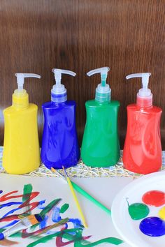 four different colored soap dispensers sitting on a table next to art supplies