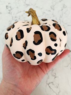 a hand holding a white and brown painted pumpkin with black spots on it's face