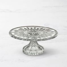 a clear glass cake plate on a white marble countertop with an intricate design in the center