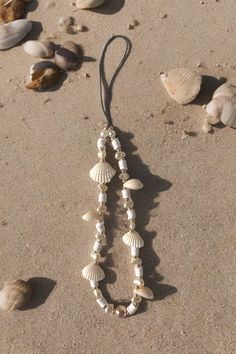 a necklace with shells hanging from it's side on the sand next to seashells