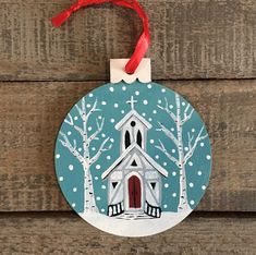 a christmas ornament with a church in the snow and red ribbon hanging from it