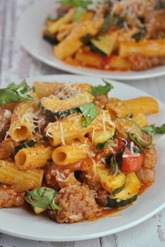 two white plates filled with pasta and meat covered in sauce, cheese and basil leaves