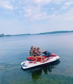 four people riding on the back of a red and white jet ski