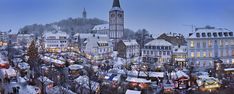 a city with lots of christmas trees and lights on it's buildings in the snow