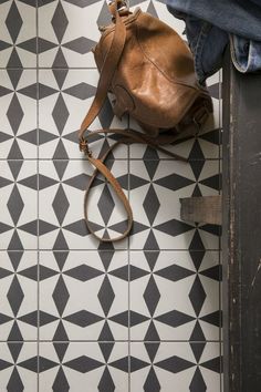 a brown purse sitting on top of a black and white floor next to a pair of jeans