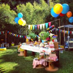 an outdoor party with balloons and cake on the table in front of flags, bunting and potted plants