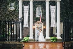 a bride and groom standing in front of an old brick building with columns on either side