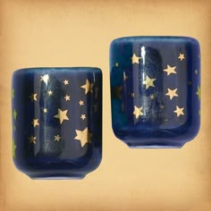 two blue cups with gold stars on them sitting side by side in front of a beige background