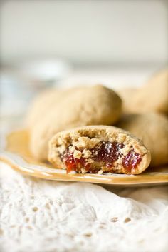 some cookies are on a plate and one has jelly in the middle with crumbs