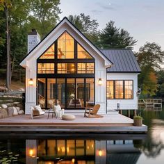 a small white house sitting on top of a lake next to a dock with chairs