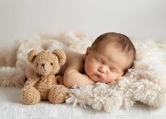 a baby sleeping next to a teddy bear on a white blanket with it's eyes closed