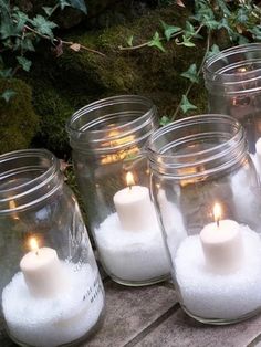 several mason jars filled with white sand and lit candles