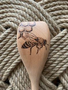 a wooden spoon with a drawing of a honeybee on it sitting next to some yarn