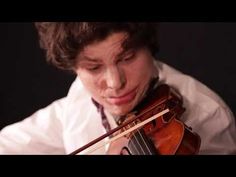 a young man is playing the violin in front of his face and looking down at it